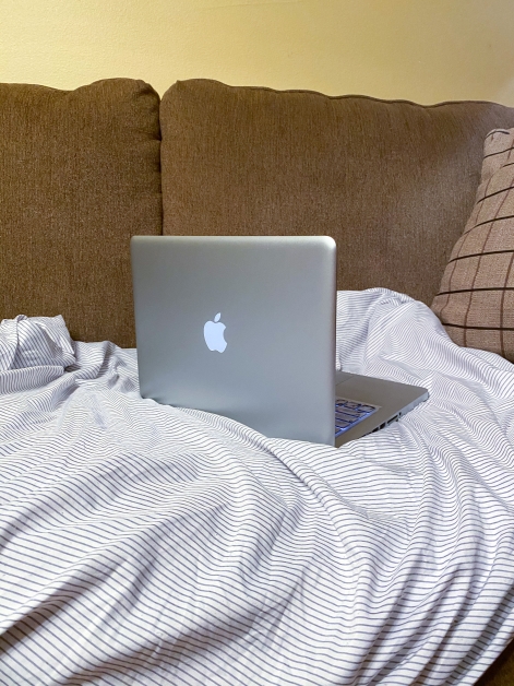 Mac laptop resting on top of a striped sheet on a brown couch