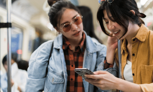 two women talking on a subway and looking down at a cell phone