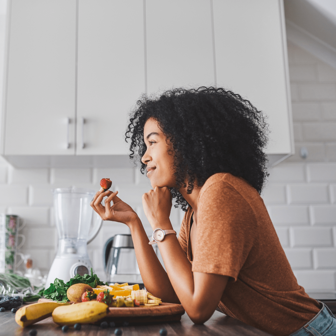 happy woman standing in kitchen eating healthy food
