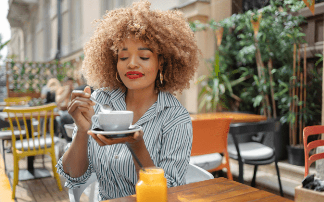 black woman with curly hair enjoying cappuccino in a street cafe