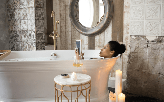black woman reading a book while taking a bath with champagne and candles