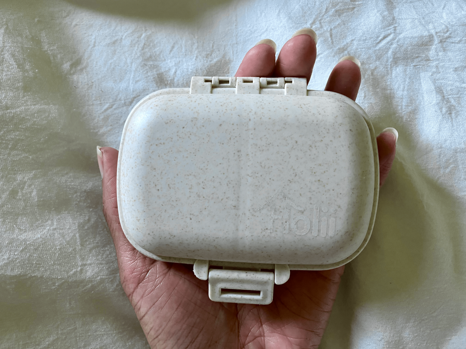 hand holding a small beige travel pill case