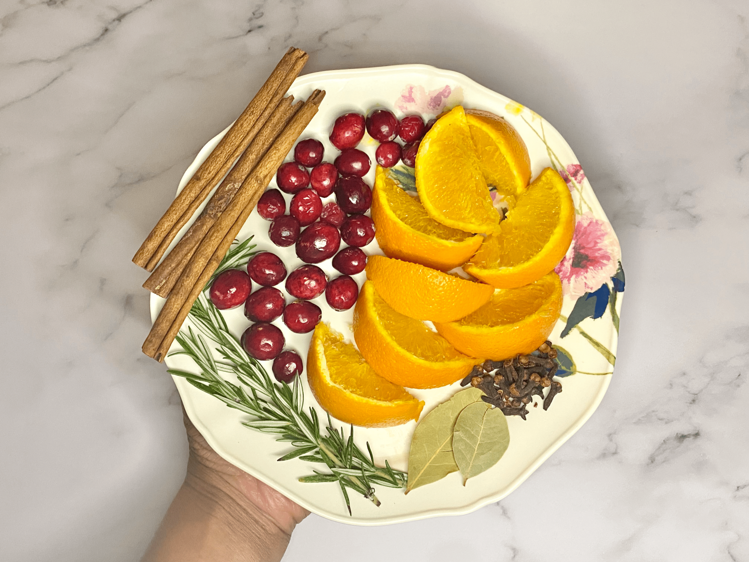 colorful plate with orange slices, bay leaves, sprigs of rosemary, cinnamon sticks, cranberries, and whole cloves