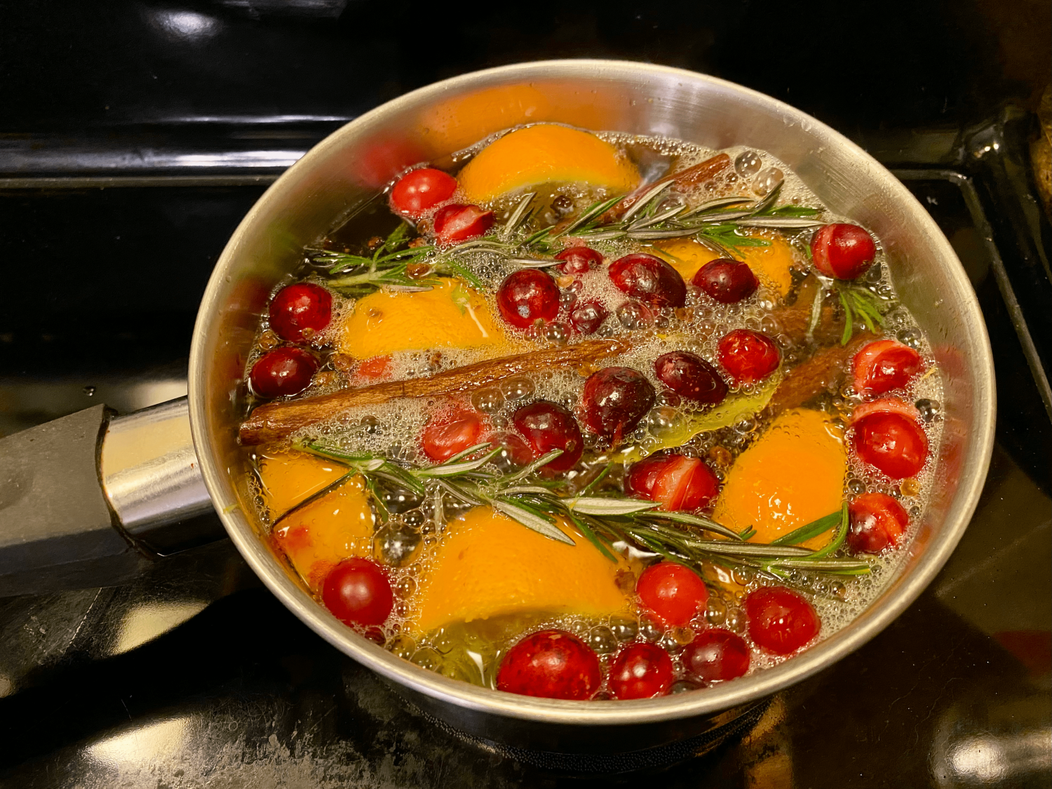 boiling pot filled with water, orange slices, bay leaves, sprigs of rosemary, cinnamon sticks, cranberries, and whole cloves