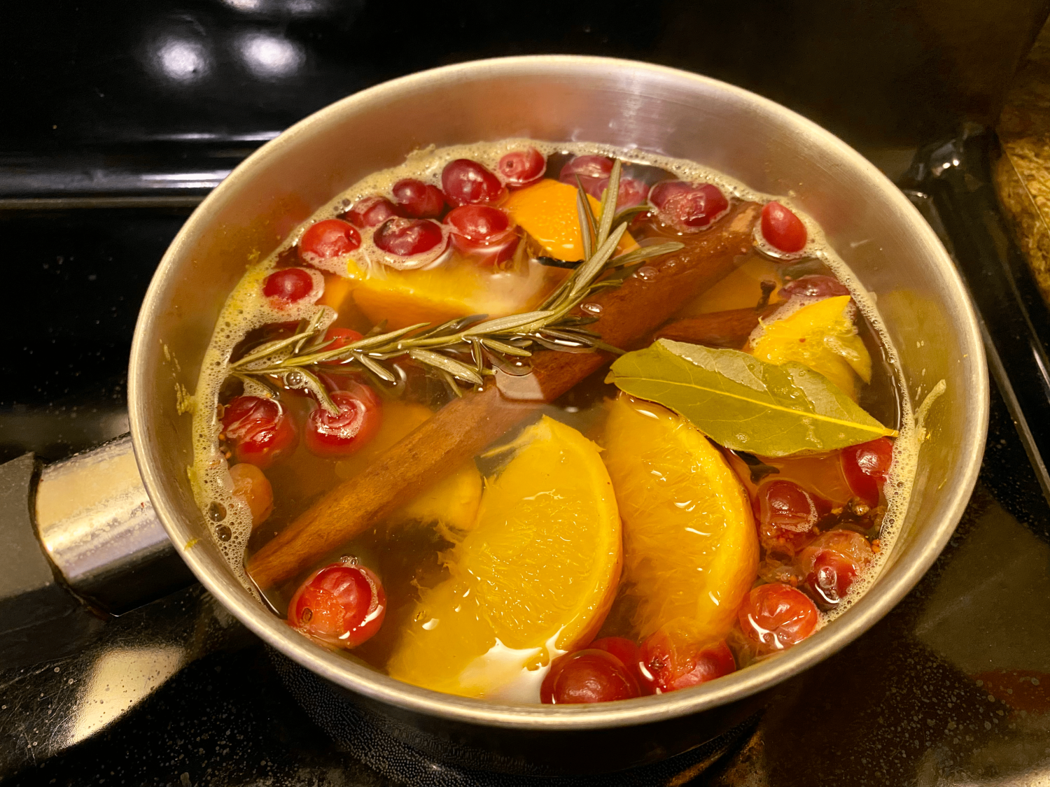 simmering pot filled with water, orange slices, bay leaves, sprigs of rosemary, cinnamon sticks, cranberries, and whole cloves