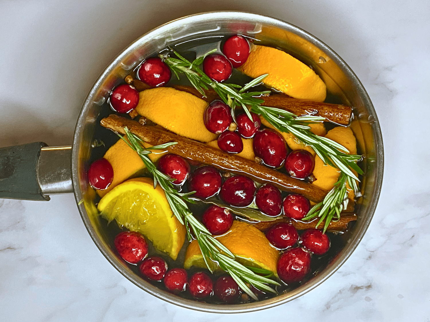 pot filled with water, orange slices, bay leaves, sprigs of rosemary, cinnamon sticks, cranberries, and whole cloves