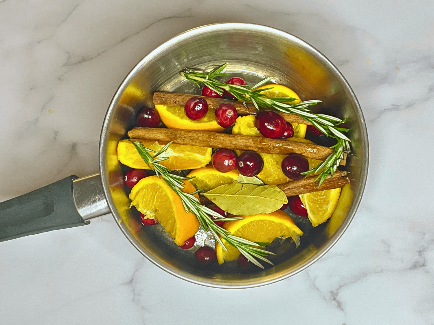 pot filled with orange slices, bay leaves, sprigs of rosemary, cinnamon sticks, cranberries, and whole cloves